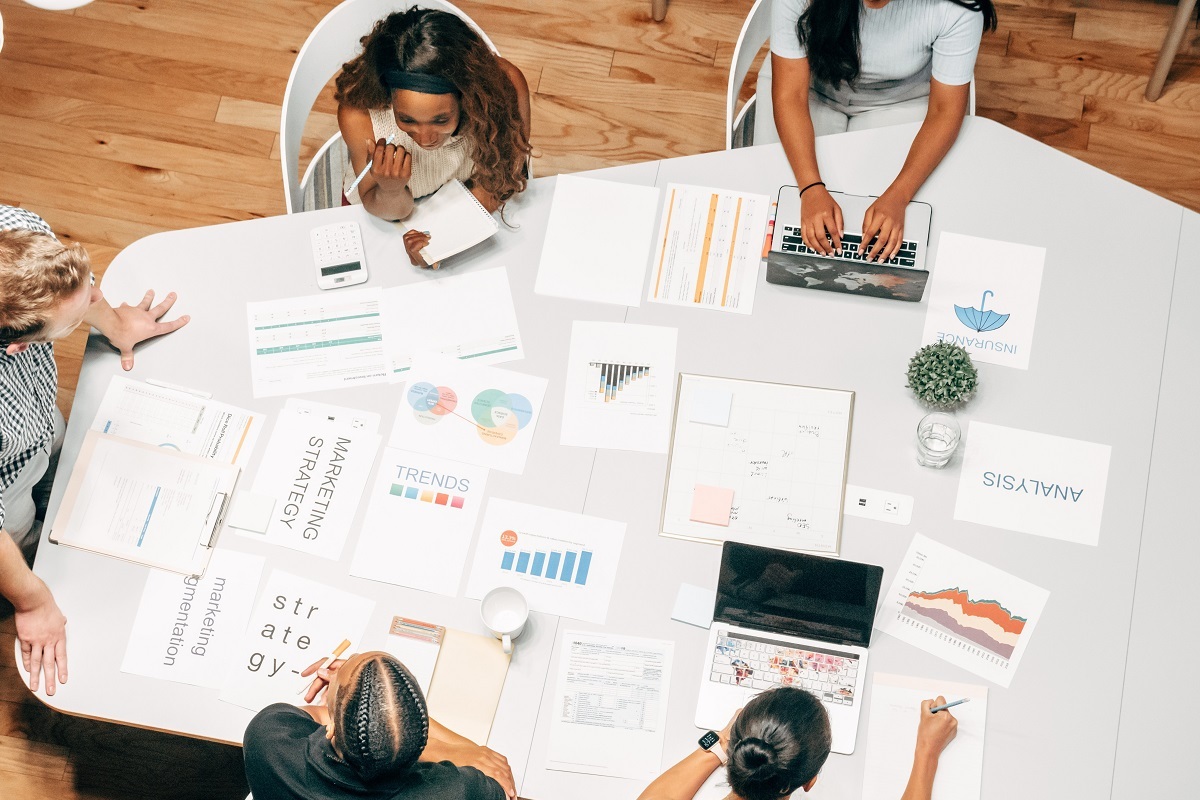 pessoas analisando relatórios em reunião: plano de marketing pessoas sentadas em uma mesa grande de reunião, analisando uma série de relatórios espalhados