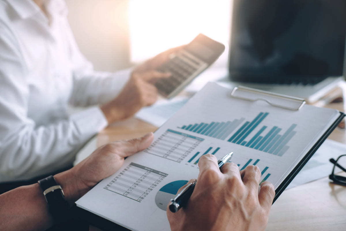 pessoas analisando relatórios: ROI pessoas sentadas analisando diversos relatórios e, uma delas, está com uma calculadora na mão