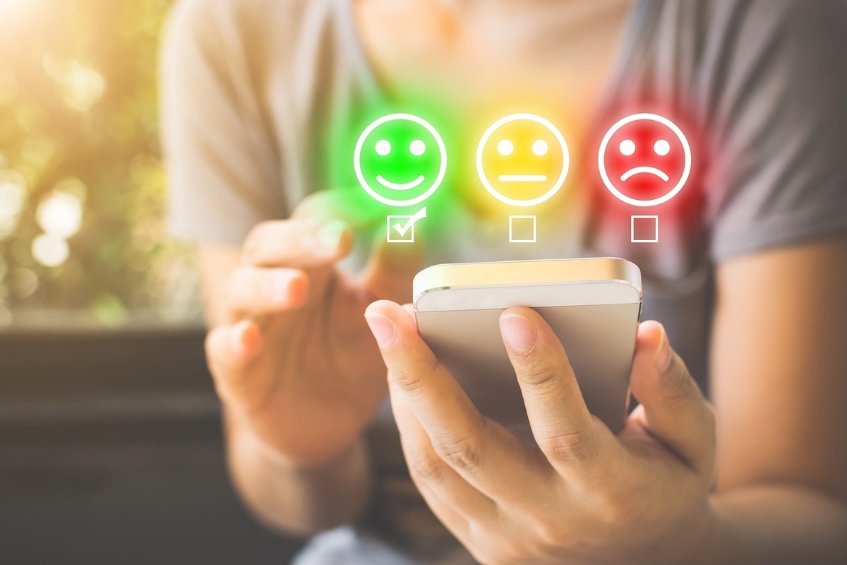 pessoa usando o celular: SEO local pessoa usando o celular e, no meio da imagem há 3 carinhas representando uma pesquisa de satisfação. Enquanto uma carinha está feliz, outra está apática e outra triste