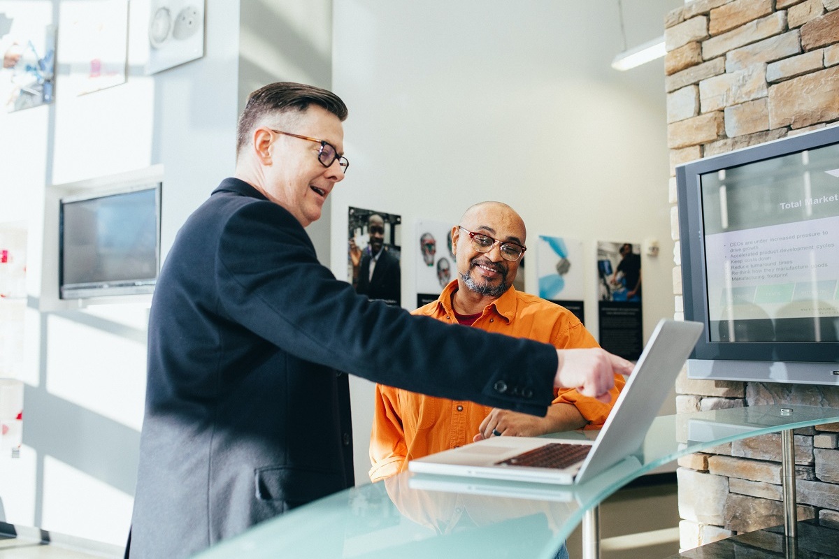 homens conversando: guia de vendas dois homens conversando, enquanto um deles aponta o dedo para um notebook aberto