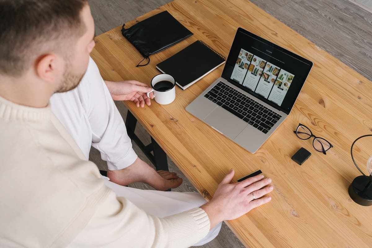 homem trabalhando: guia de vendas homem em sua mesa de trabalho com um laptop, caderno, óculos e caneca de café