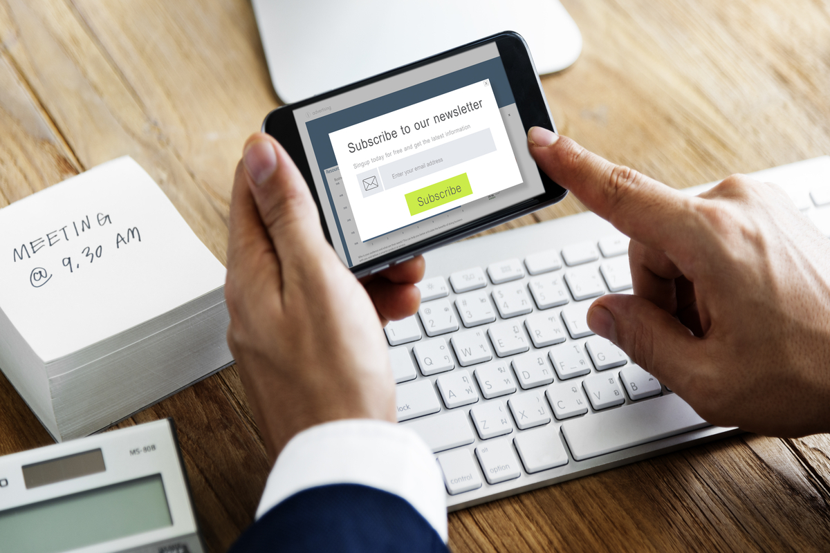 homem se inscrevendo em uma newsletter: inbound marketing homem sentado com um celular na mão, acessando a página de uma newsletter