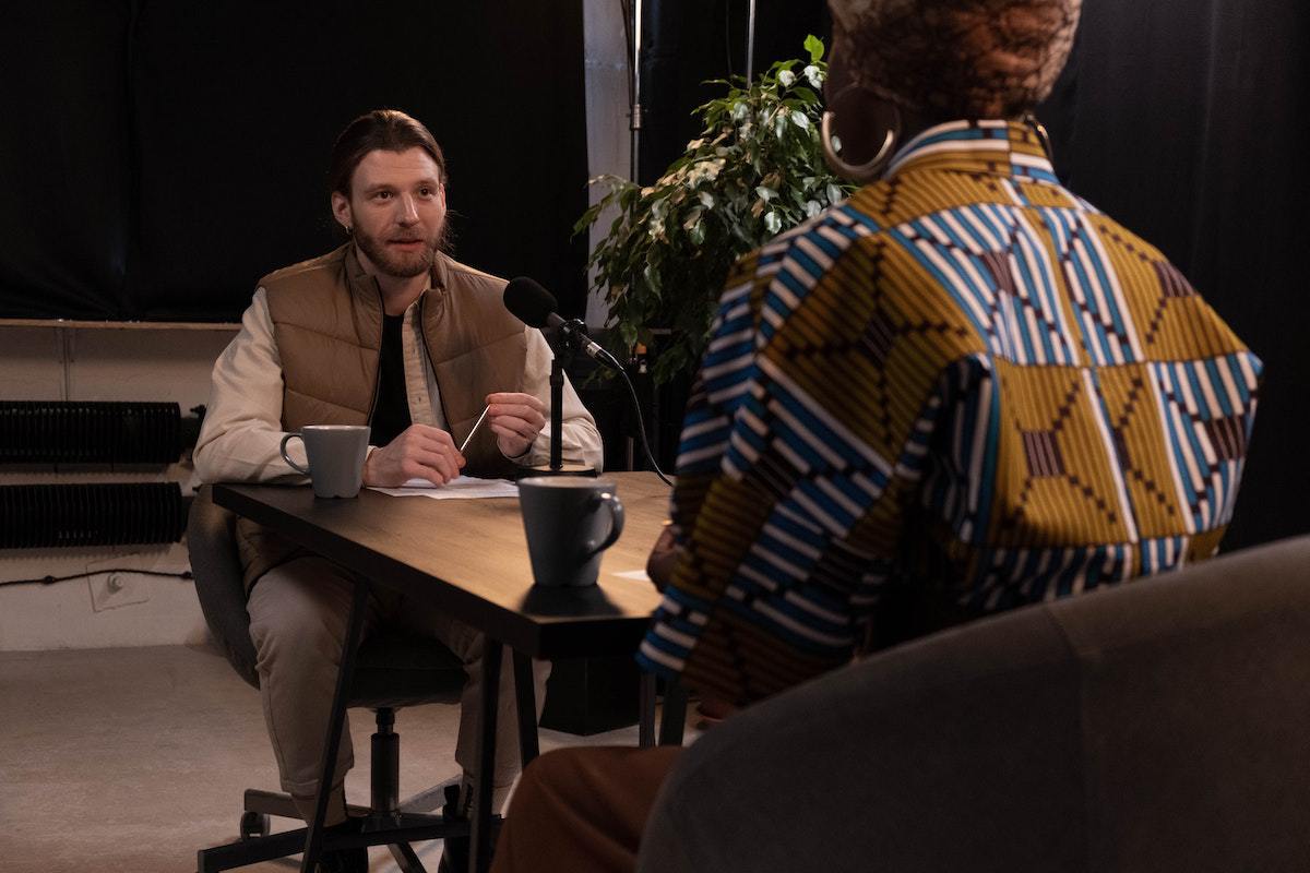 homens conversando: podcasts dois homens sentados um de frente para o outro. Eles estão conversando de forma descontraída e há um microfone na frente de cada um deles