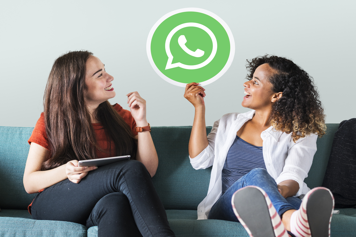foto com a logo do WhatsApp: redes sociais duas mulheres sentadas em um sofá, enquanto uma delas segura a logo do WhatsApp