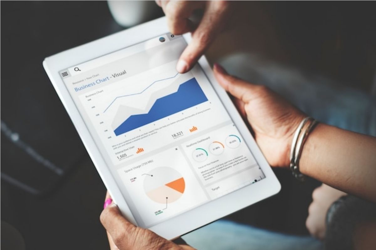 pessoas usando um tablet: SEO duas pessoas analisando gráficos em um tablet. Enquanto uma segura o dispositivo com as mãos, a outra aponta o dedo para a tela dele