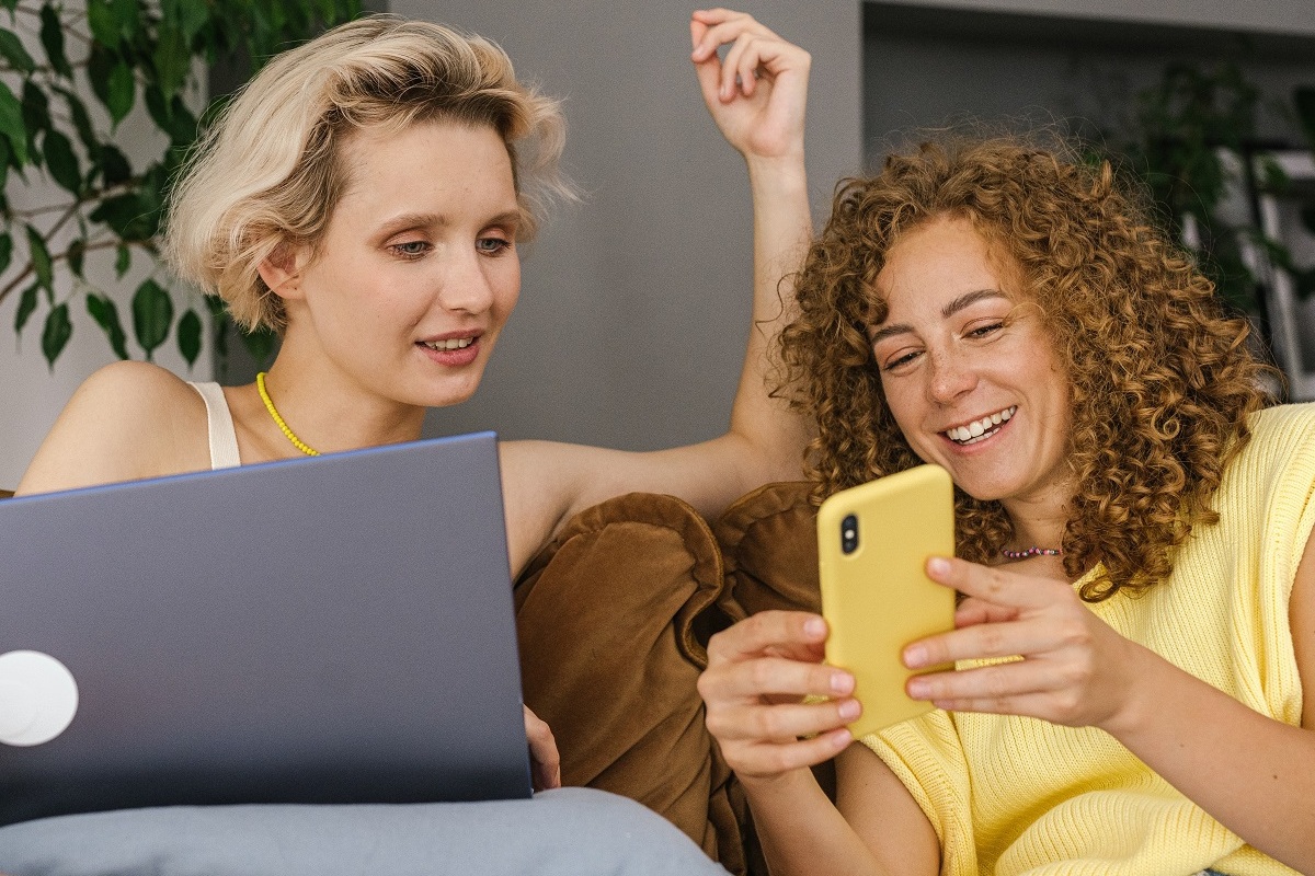 mulheres conversando: escaneabilidade duas mulheres sentadas de forma despojada, uma com um celular e outra com laptop no colo. Elas parecem estar conversando