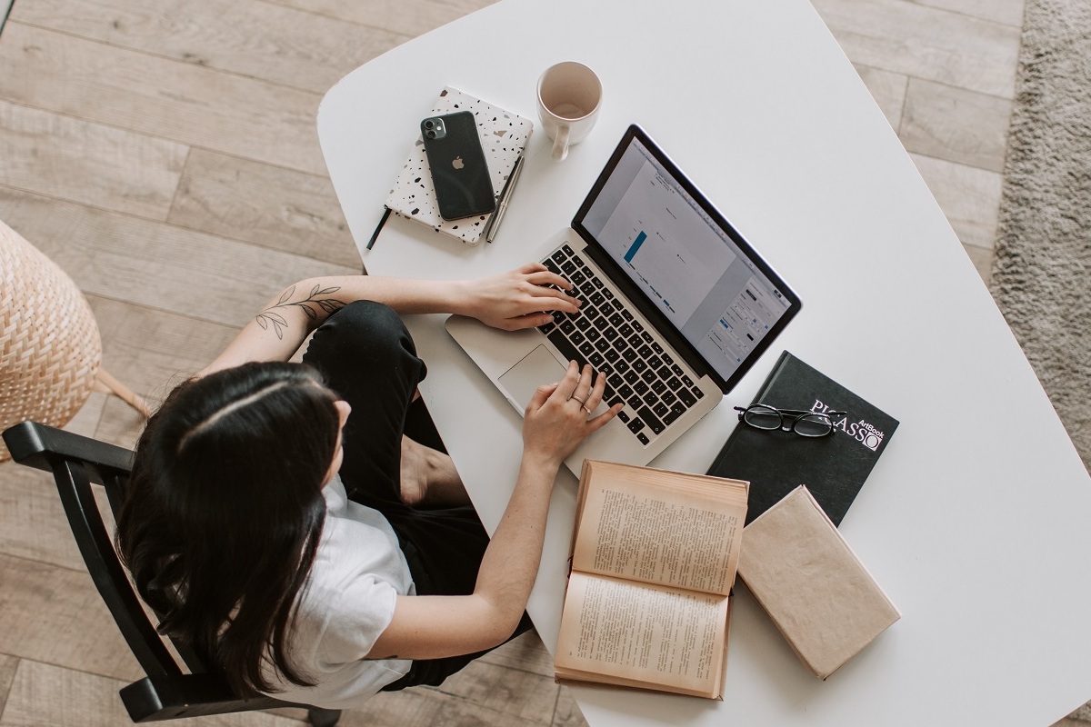 mulher trabalhando no computador: google EAT mulher sentada trabalhando em seu laptop em cima da mesa. Nessa última também há livros, celular e uma caneca
