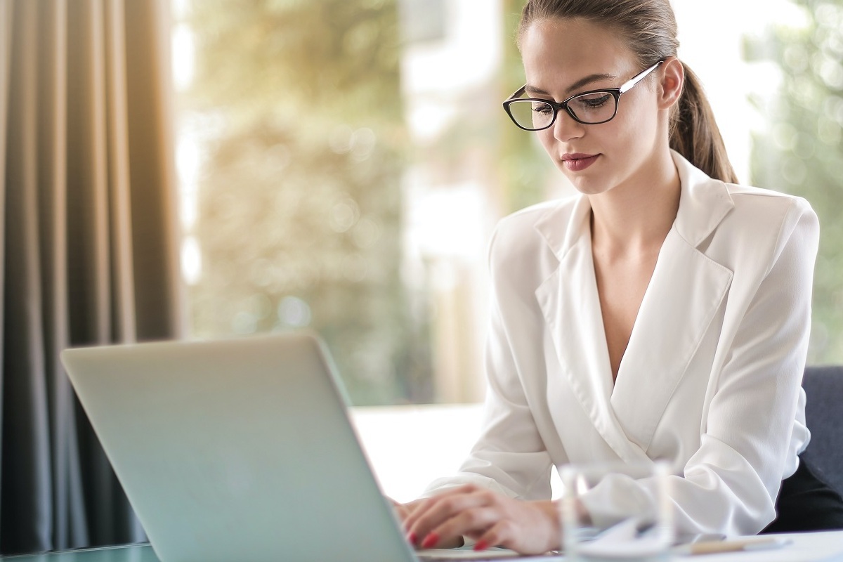 mulher trabalhando no laptop: google EAT mulher de óculos e blusa social, sentada, trabalhando em seu laptop