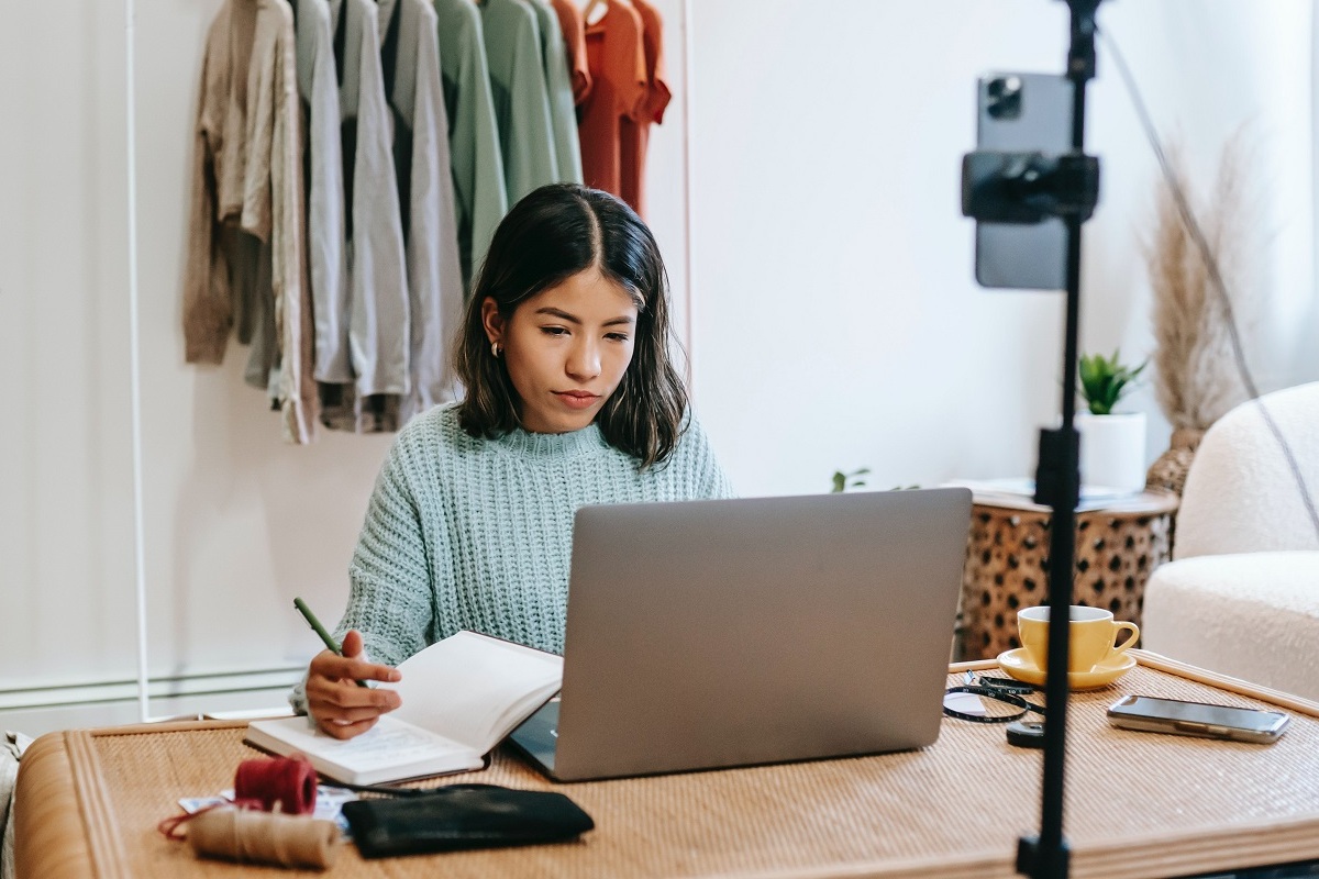 mulher escrevendo: guest post mulher sentada em frente a um laptop, enquanto anota alguma coisa no seu caderno