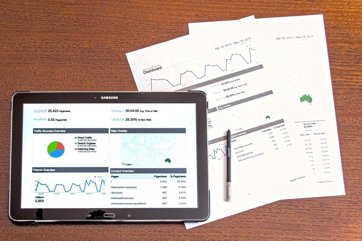 tablet com relatórios: publicidade imagem de uma mesa com um tablet mostrando vários gráficos. Na mesa tem também vários relatórios em forma de folha de papel