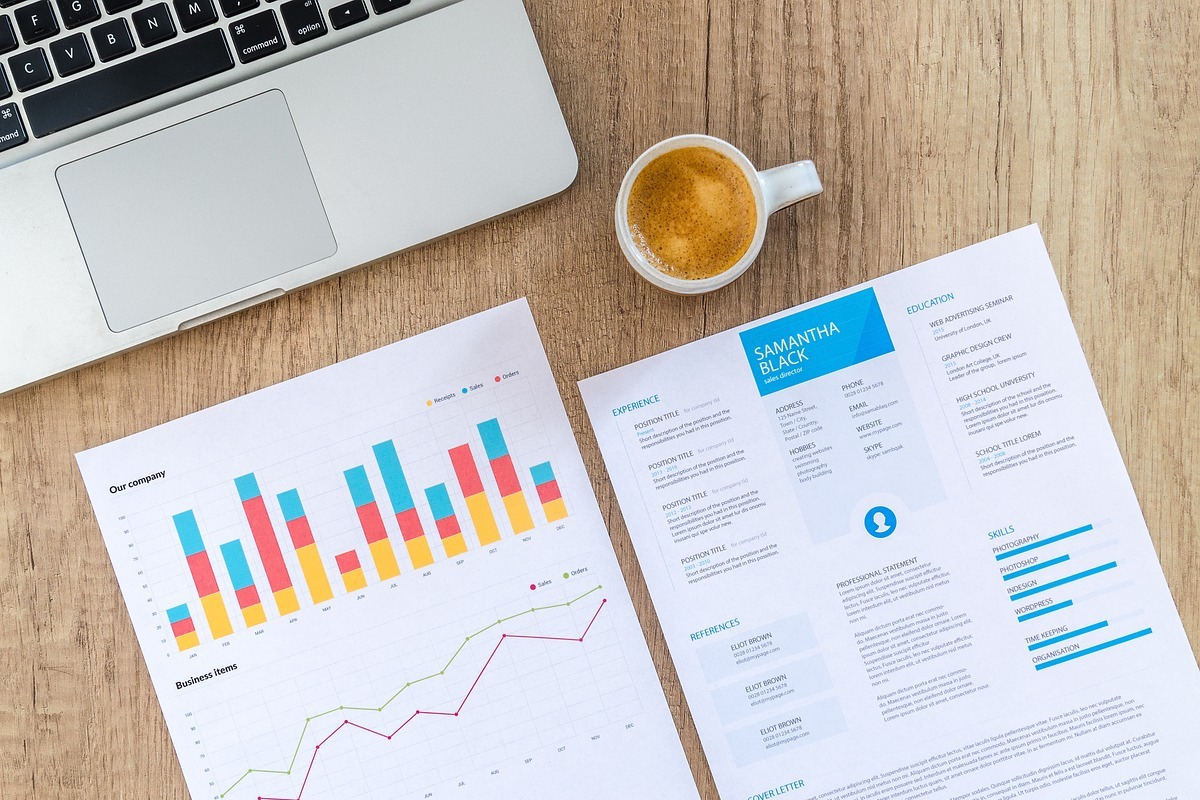 relatórios: whatsapp business notebook em cima da mesa, com vários relatórios do lado e uma caneca de café