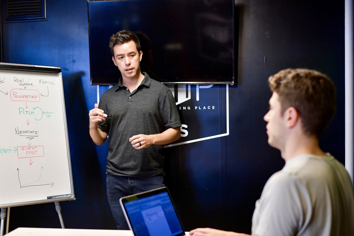 homens em reunião: bert homem em pé explicando alguma coisa para um homem sentado com um laptop à sua frente