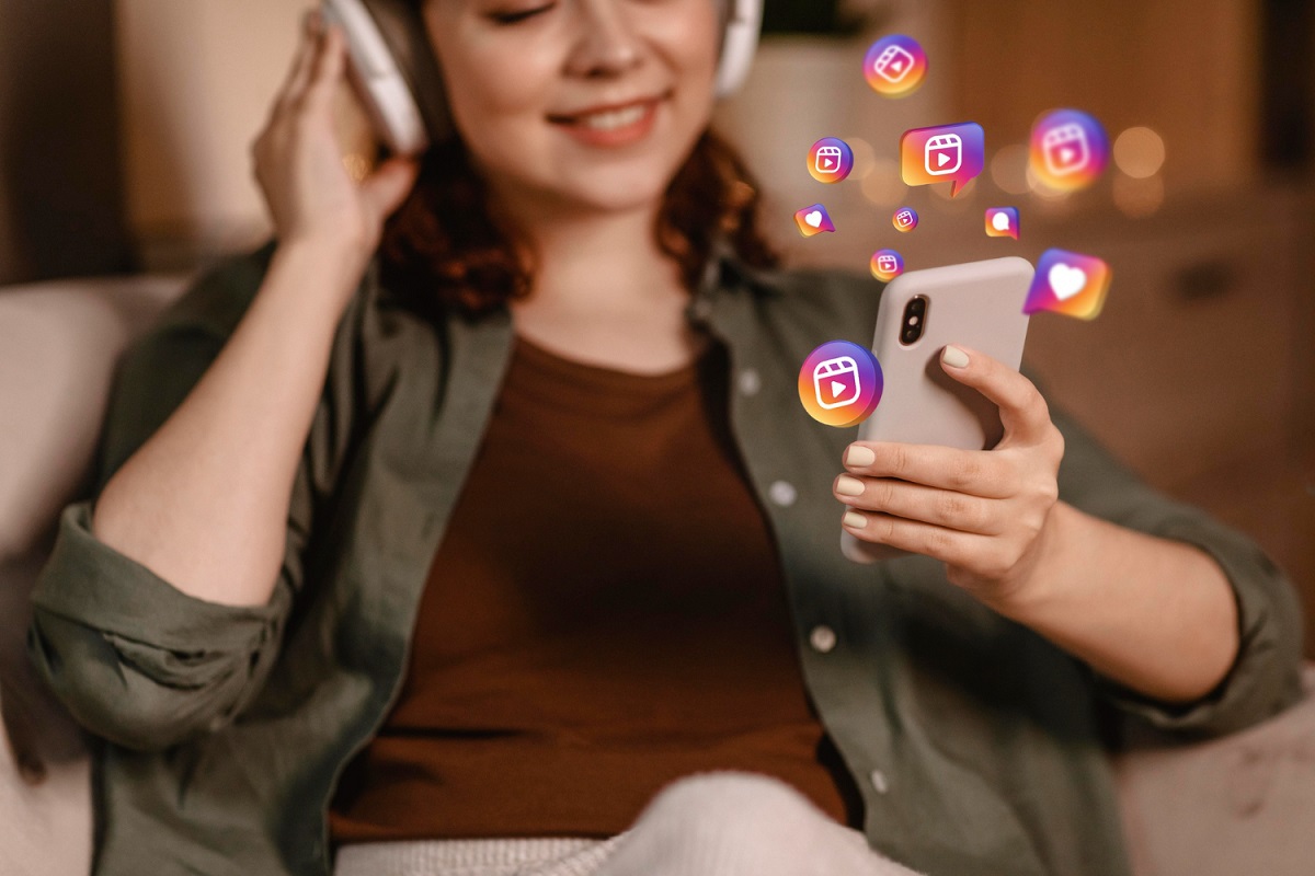 mulher usando o celular: como ganhar seguidores no instagram mulher sentada, com um headset, usando o celular. Na imagem tem vários símbolos que remetem ao instagram