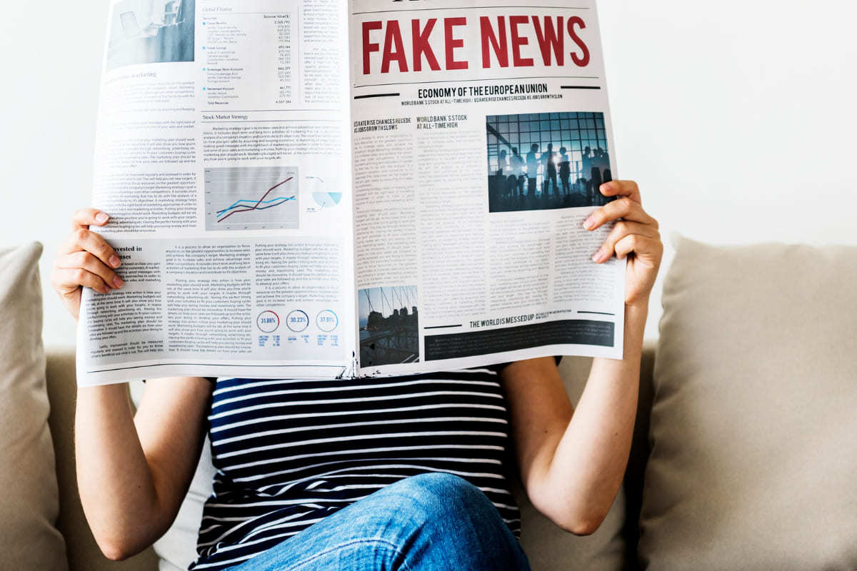 pessoa lendo: fake news pessoa sentada, lendo um jornal que, na capa, tem o nome fake news em vermelho