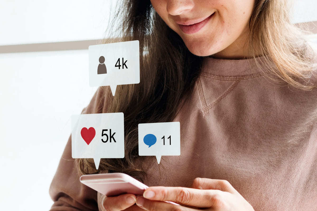 mulher usando celular: hootsuite mulher usando o celular. Na imagem aparecem vários símbolos remetendo as redes sociais