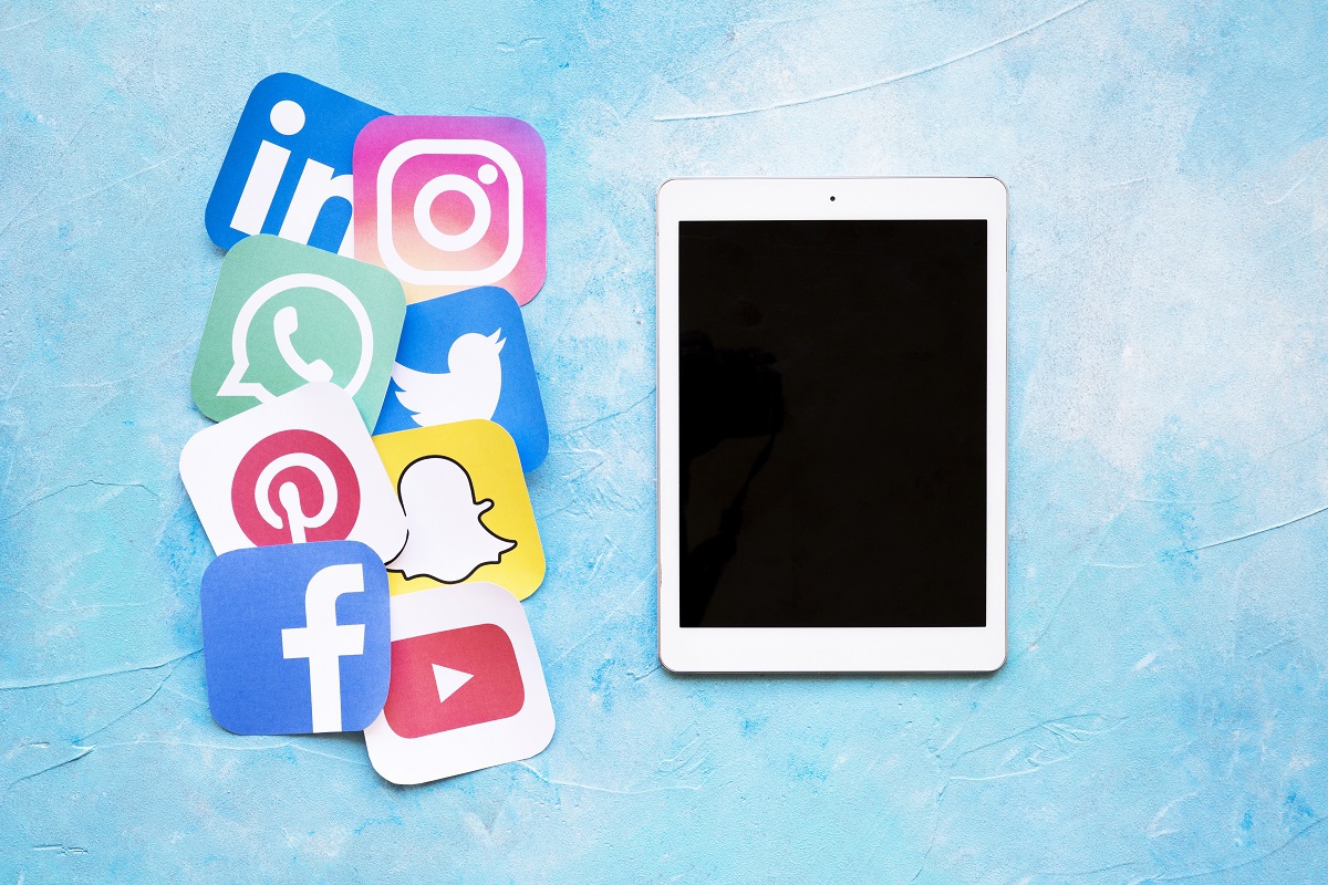 Horário de postagem ideal para Facebook, Instagram, LinkedIn, Twitter e TikTok tablet do lado de várias placas mostrando símbolos das redes sociais