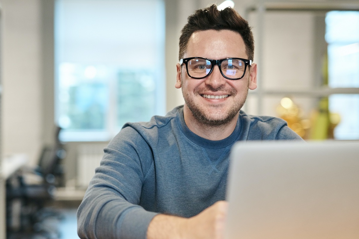 homem usando laptop: mídia interativa homem sentado de frente para um laptop, sorrindo