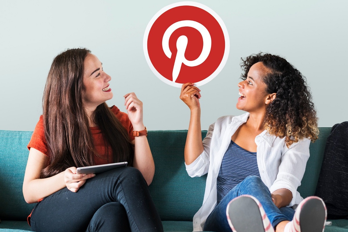 mulher segurando símbolo do pinterest duas mulheres sentadas, uma delas levantando o símbolo do pinterest