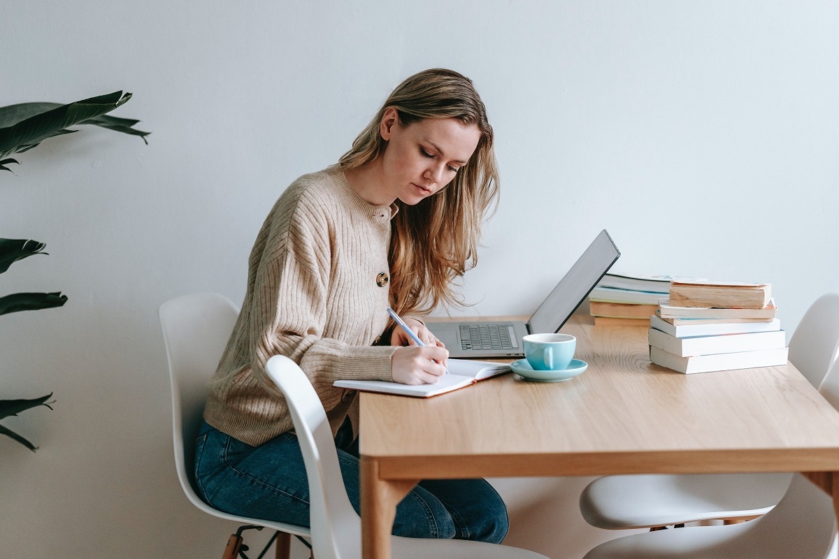 mulher trabalhando: seo off page mulher trabalhando no laptop, sentada e anotando algo em seu caderno