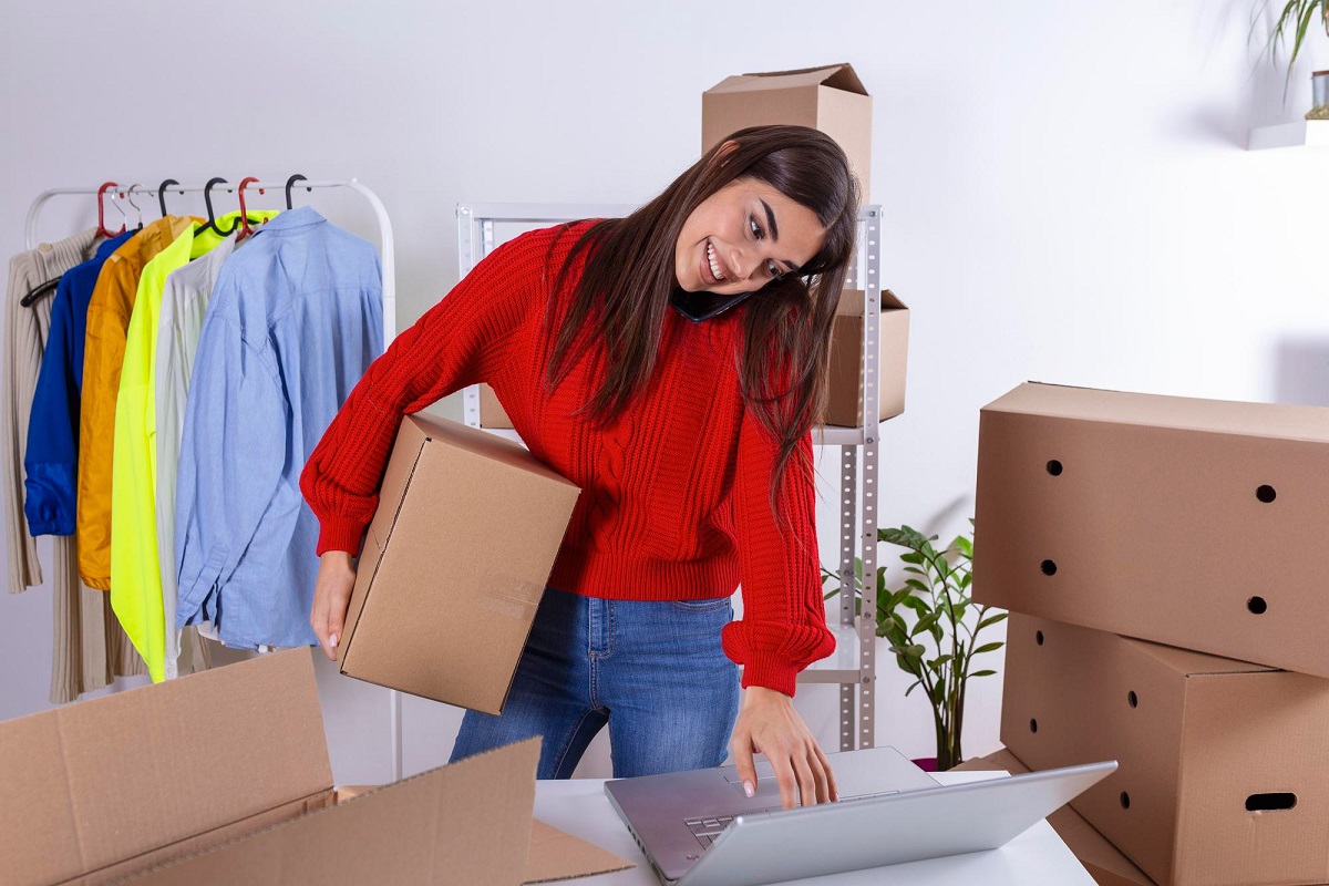mulher trabalhando: venda consignada mulher falando no telefone, enquanto segura uma caixa e mexe no laptop
