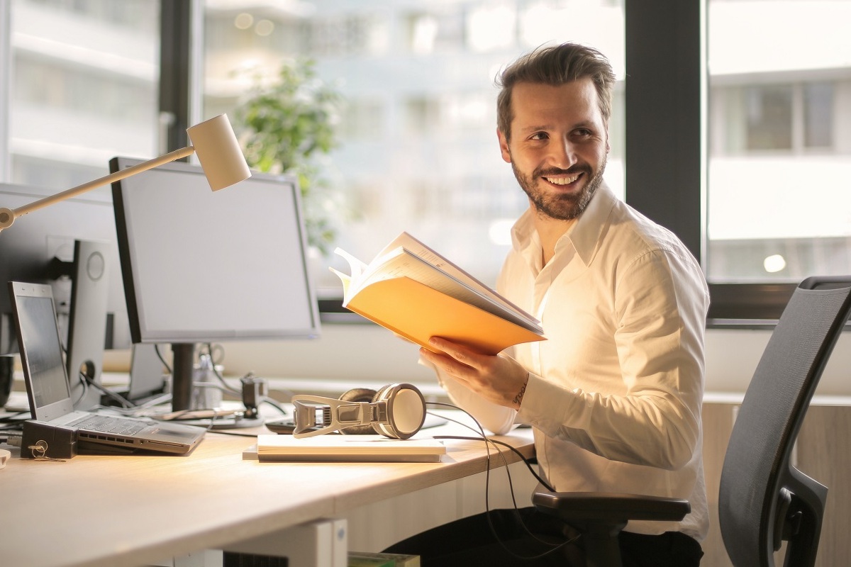 homem sorrindo: white hat homem sentado, sorrindo, com um livro na mão
