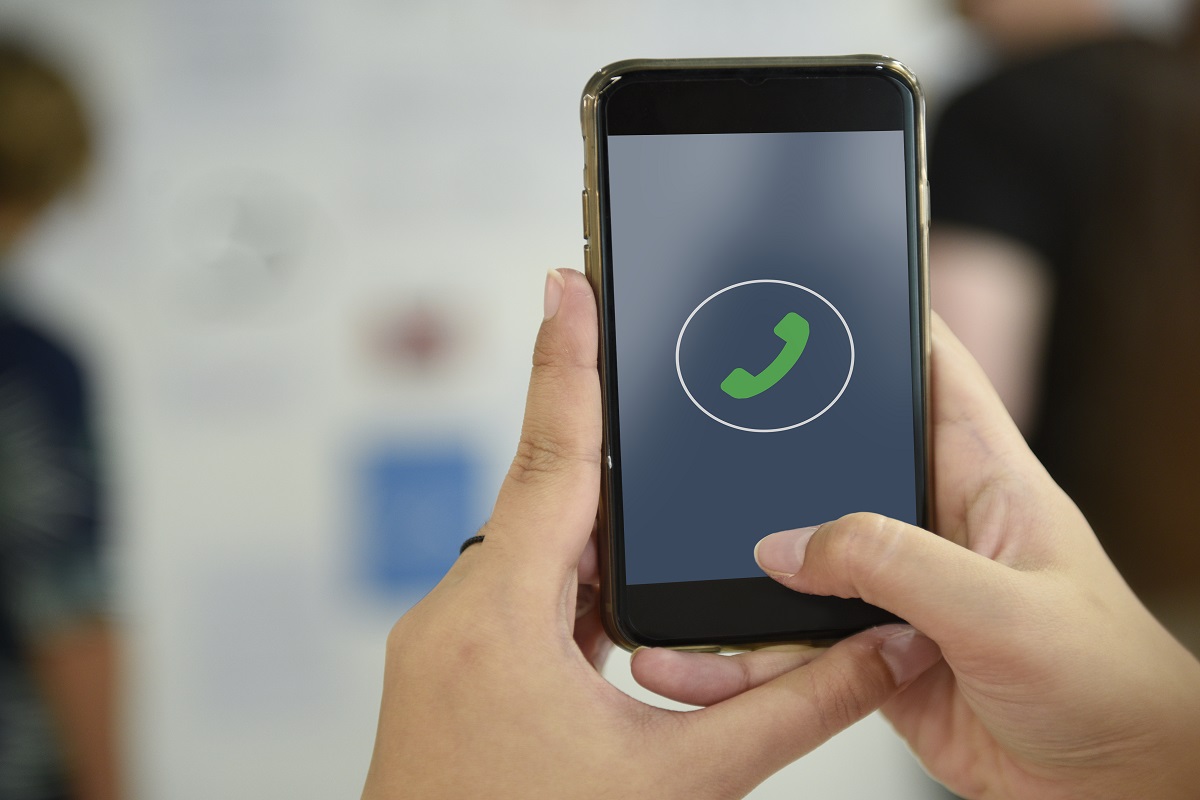 Pessoa usando o WhatsApp: Atendimento via WhatsApp Na imagem mostra uma pessoa segurando um smartphone, e na tela aparece o símbolo do WhatsApp.