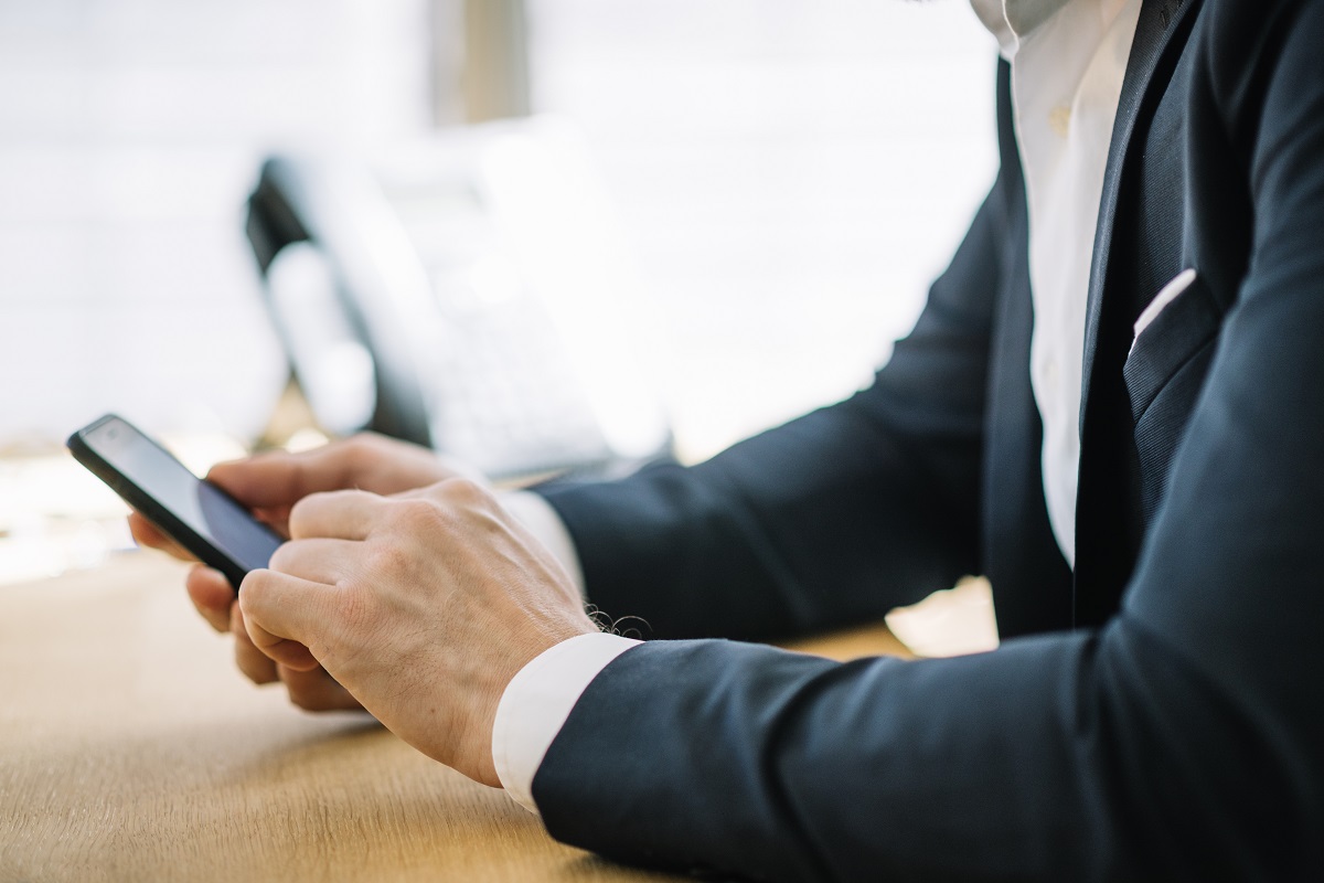 Homem de terno segurando o smartphone: Atendimento via Whatsapp Na imagem está um homem de terno segurando um smartphone.