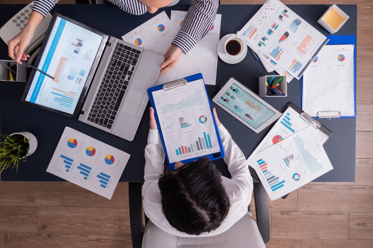 Pessoas analisando dados: ações de marketing no Instagram Pessoas em ambiente de trabalho analisando dados sobe mesa e notebook ao lado