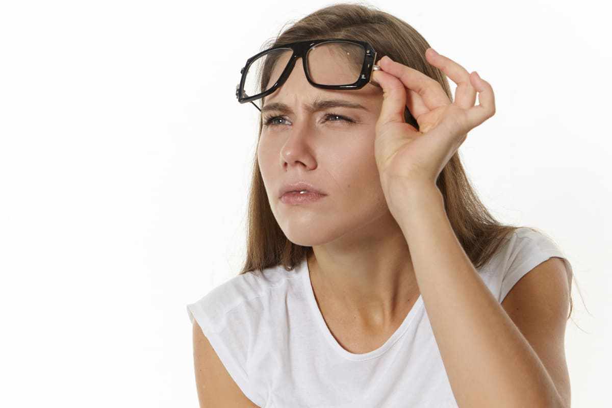 Mulher com olhos semicerrados e olhar intrigado segurando óculos levantado na testa