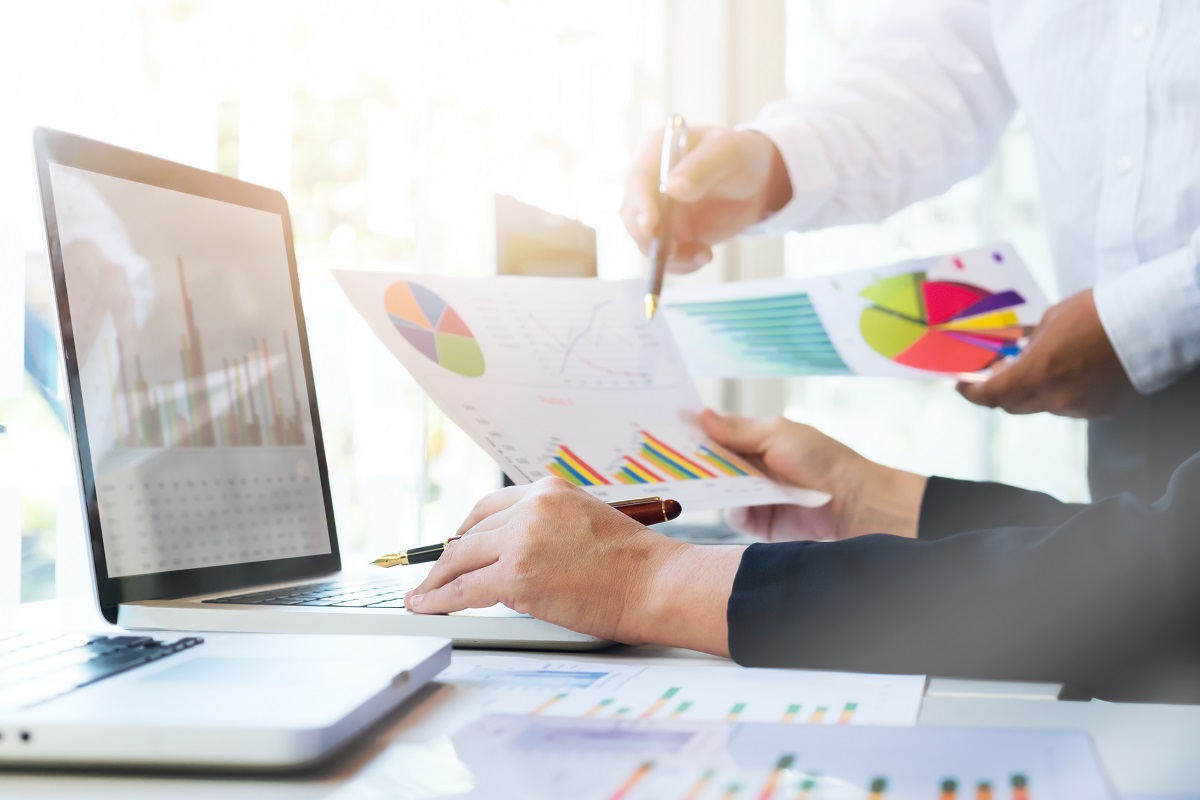 Duas pessoas analisando dados: Análise SWOT para e-commerce Imagem onde aparecem duas pessoas analisando dados em folhas de papel e gráficos na tela de um notebook,