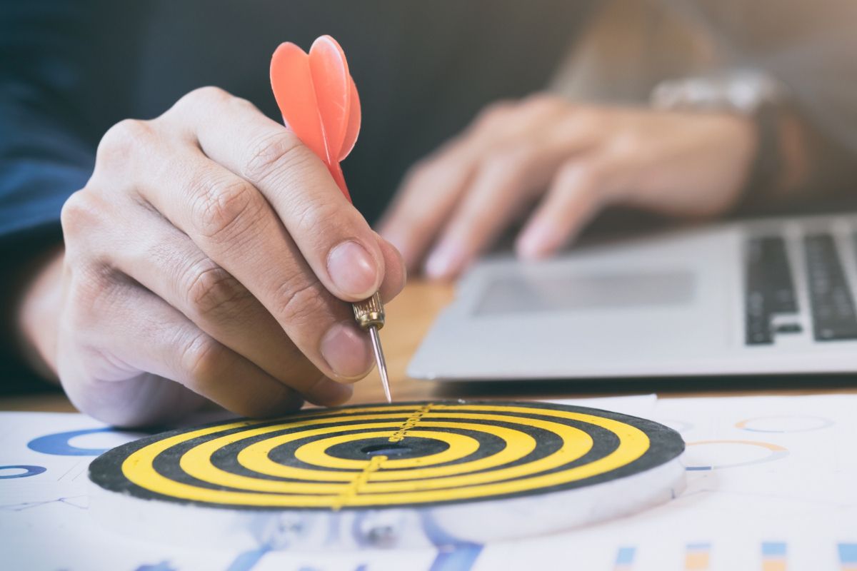 Dardo direto ao alvo: equipe de vendas Homem com dardo na mão enquanto aponta para alvo posicionado ao lado do notebook que está diante dele
