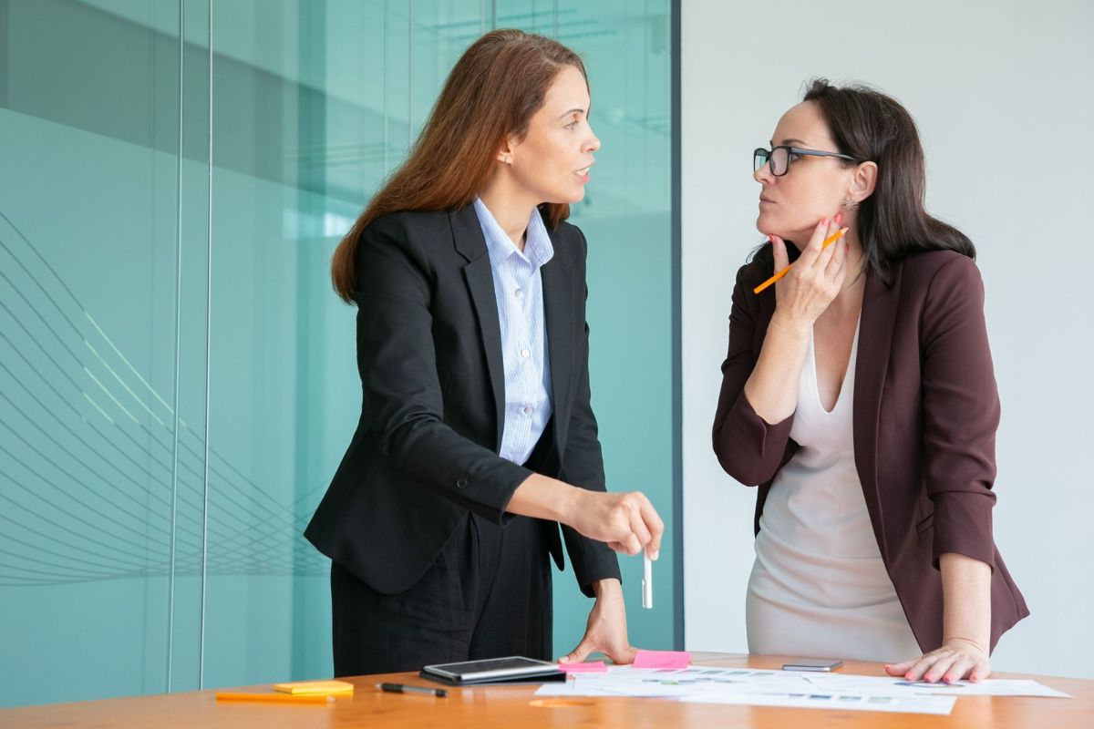 Mulheres de negócios discutindo situação em trabalho com papéis sobre mesa de madeira