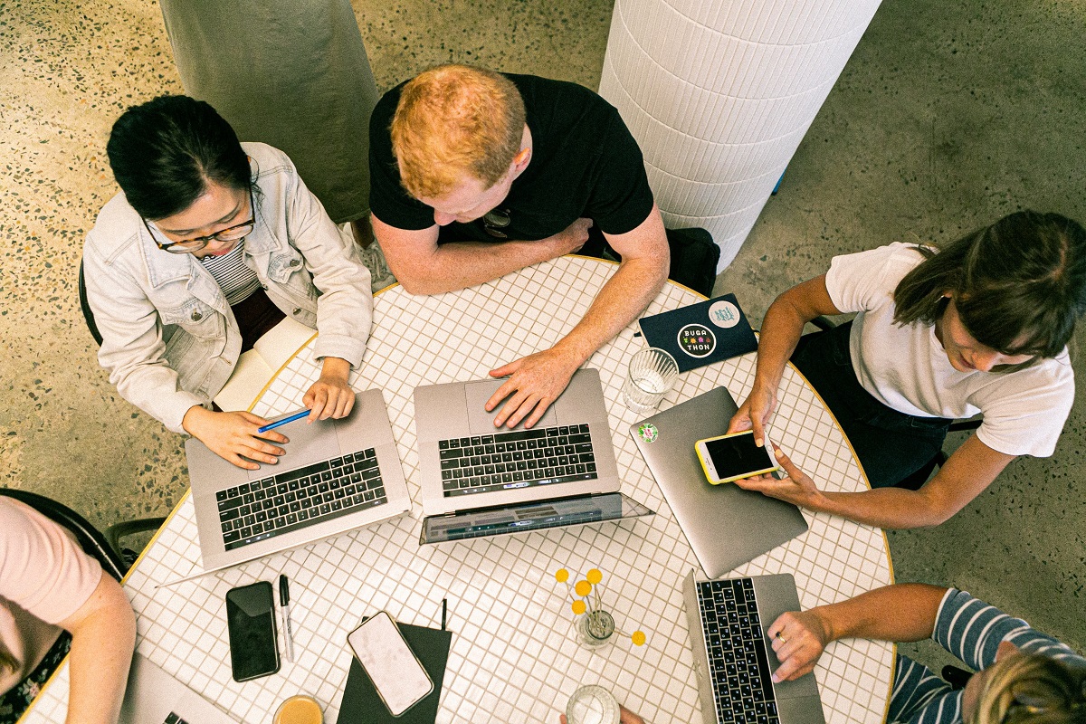 Reunião de trabalho: mitos do Marketing digital Pessoas reunidas ao redor de mesa com notebooks e smartphones debatendo tema de trabalho