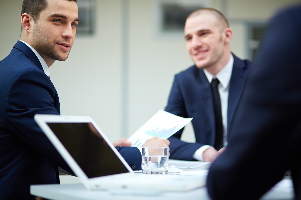 Homens debatendo negócios: persuasão Homens de terno em debate de negócio em mesa branca de trabalho com notebook branco sobre ela