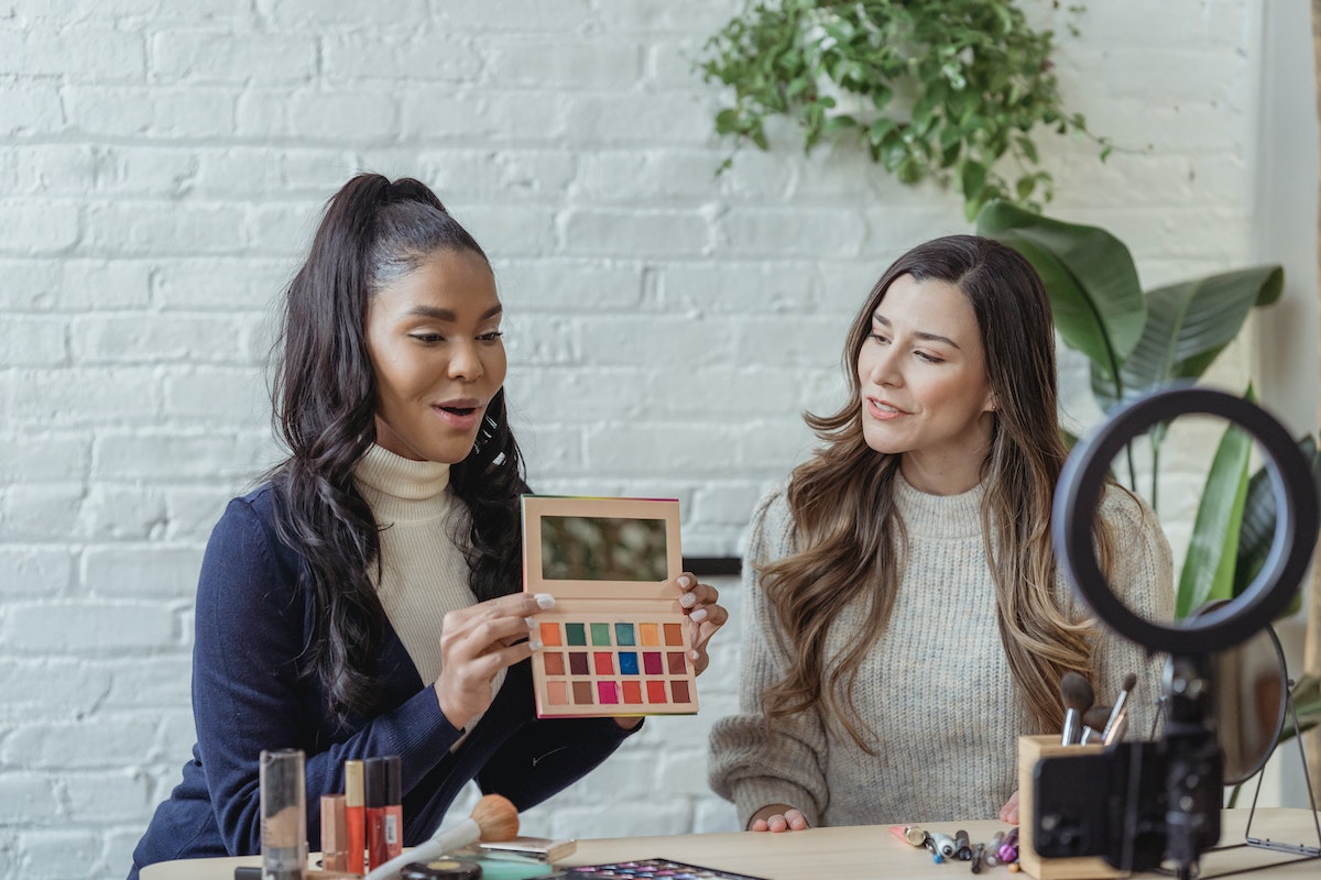 influenciadoras: plataforma de influenciadores influencer com um kit de maquiagem na mão ao lado de uma convidada