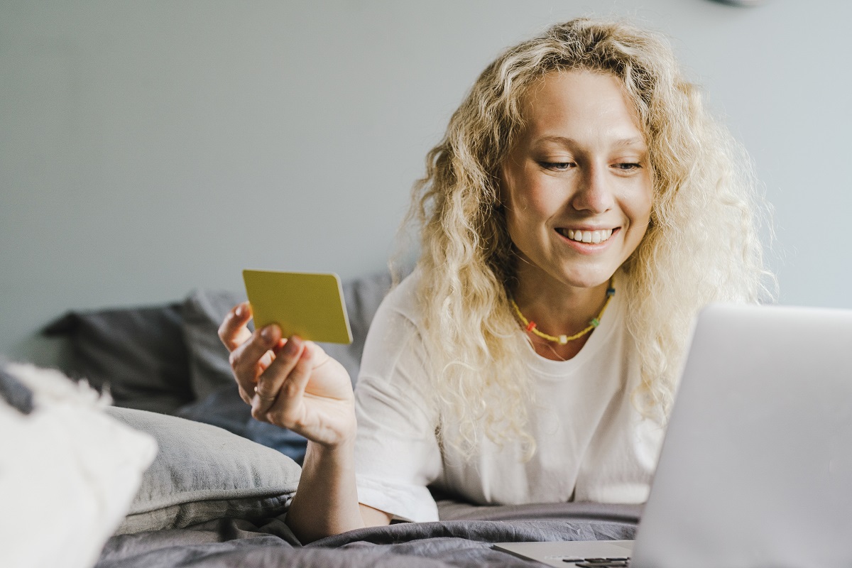 Mulher com cartão: psicologia do inbound marketing Mulher sorri enquanto vê algo em seu notebook com cartão de crédito amarelo nas mãos
