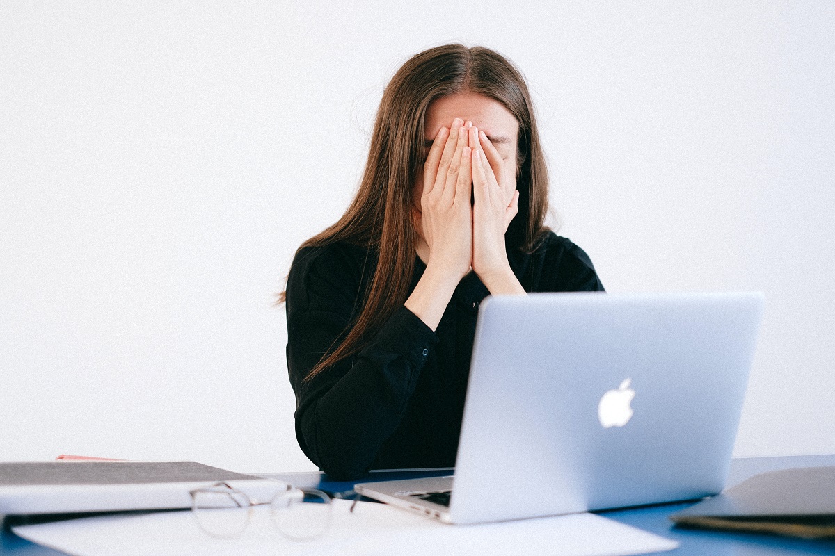 mulher de frente para um laptop, com a mão no rosto, dando aspecto de cansada