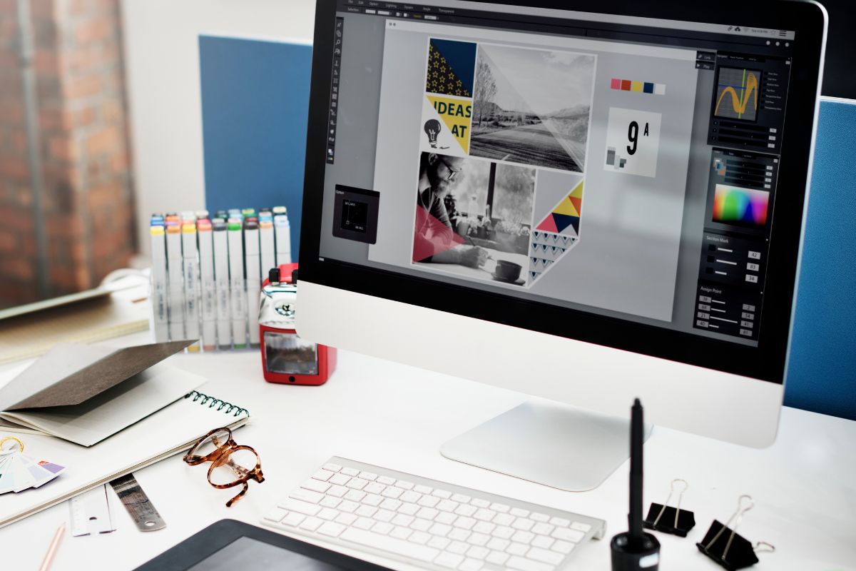 Criação de arte: colocar produtos no Instagram Computador em mesa de trabalho ao lado de cadernos para auxiliar criação de artes e o monitor exibe trabalho com montagem de arte para produto