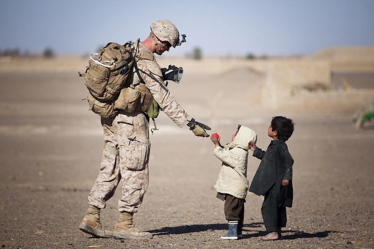 soldado interagindo com crianças: marketing social soldado dando uma bola para duas crianças