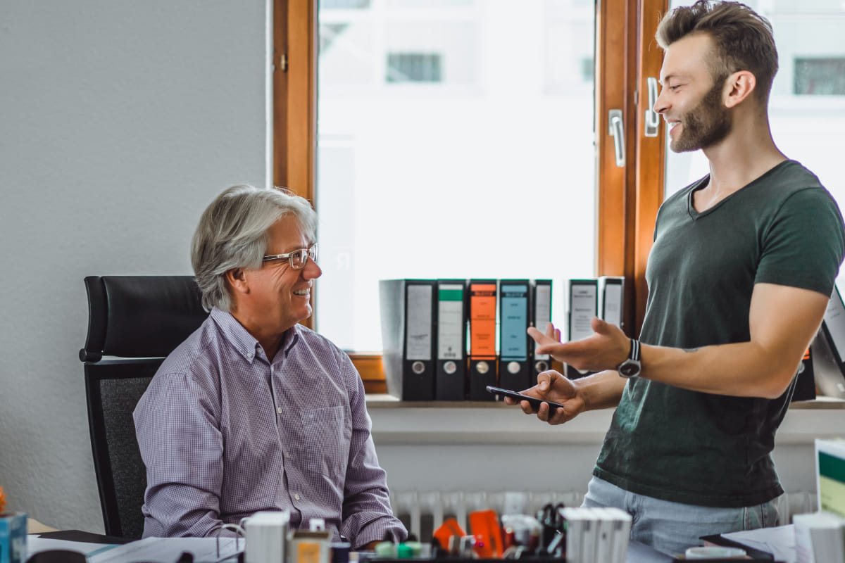 homem mais jovem de pé conversando com homem mais velho que está sentado
