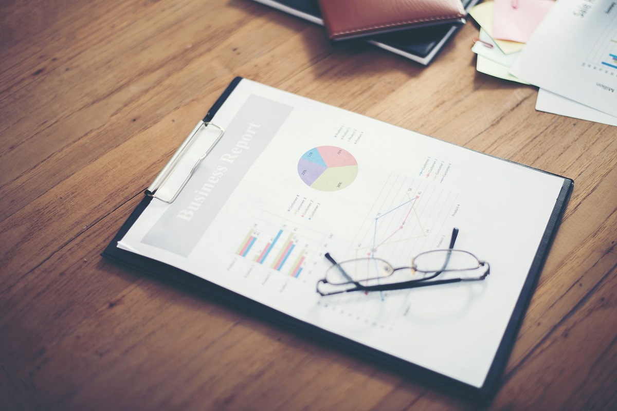 prancheta com folhas de relatórios em cima de mesa de madeira e óculos dobrado em cima dela