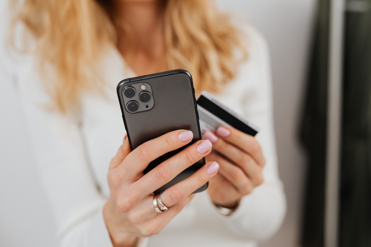 Mulher de camisa social branca de botão segurando celular com mão esquerda e cartão de crédito na outra