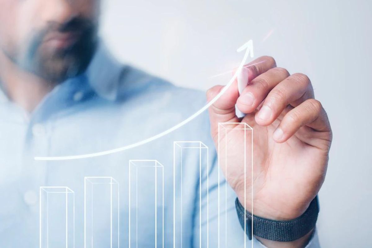 Gráfico em subida: alavancar vendas Homem usando camisa social azul e relógio de pulseira preta em couro no braço esquerdo faz desenho de gráfico em ascensão no ar em montagem