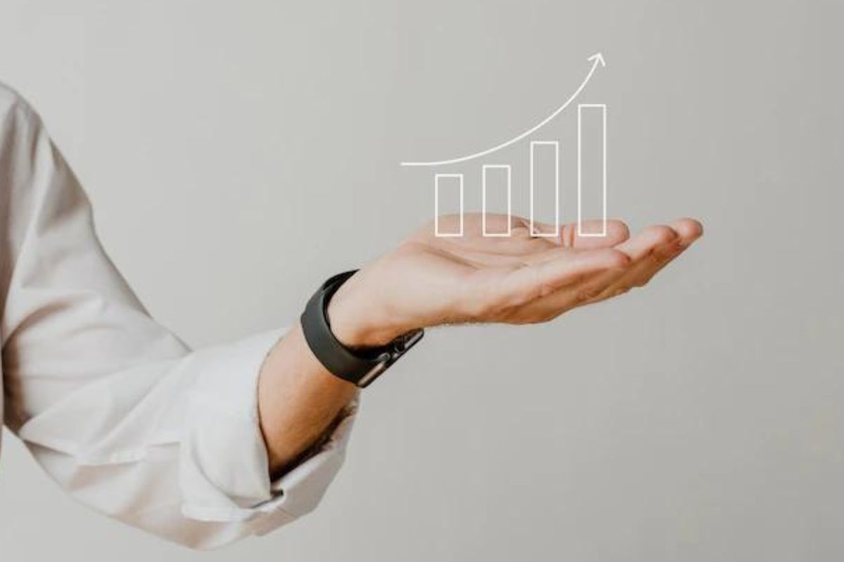 Homem com camisa branca de botão e relógio preto no punho esquerdo com mão erguida e palma para cima mostrando gráfico em ascensão desenhado no ar em montagem fotográfica