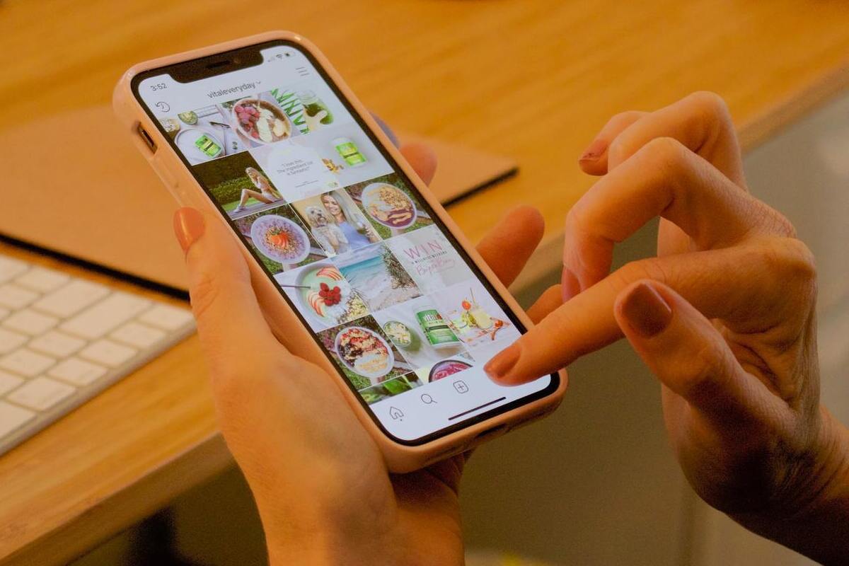 Instagram: Aplicativos de fotos Mulher usando celular diante de mesa de madeira olhando fotos no Instagram