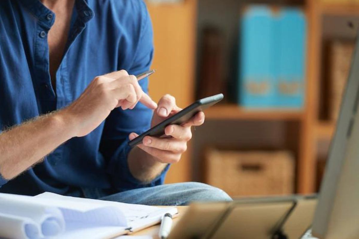 Homem usando celular sentado diante de mesa baixa com anotações em papéis à sua frente