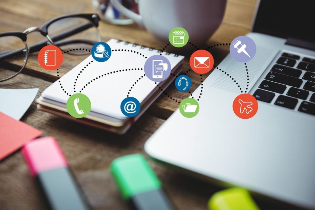 Montagem: App marketing Notebook sobre mesa e ao lado de pequeno bloco para anotações e óculos, além de caneca de café e lápis com símbolos web no ar em montagem