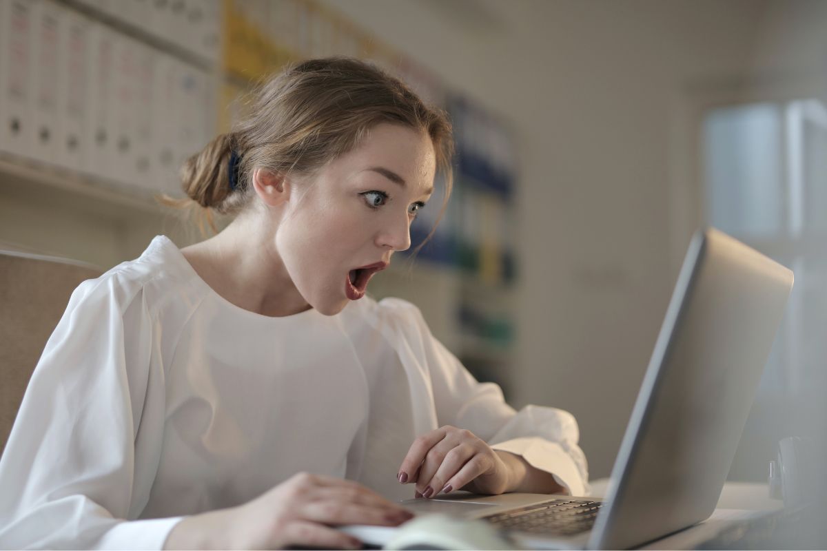 Mulher com ar e cara de surpresa ou espanto enquanto assiste algo em notebook