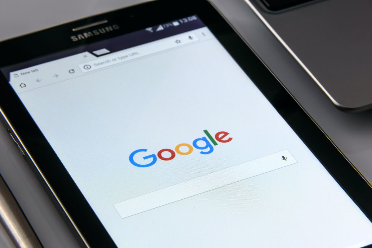 Tablet preto da Samsung ao lado de notebook cinza em cima de mesa com pesquisa Google aberta na tela