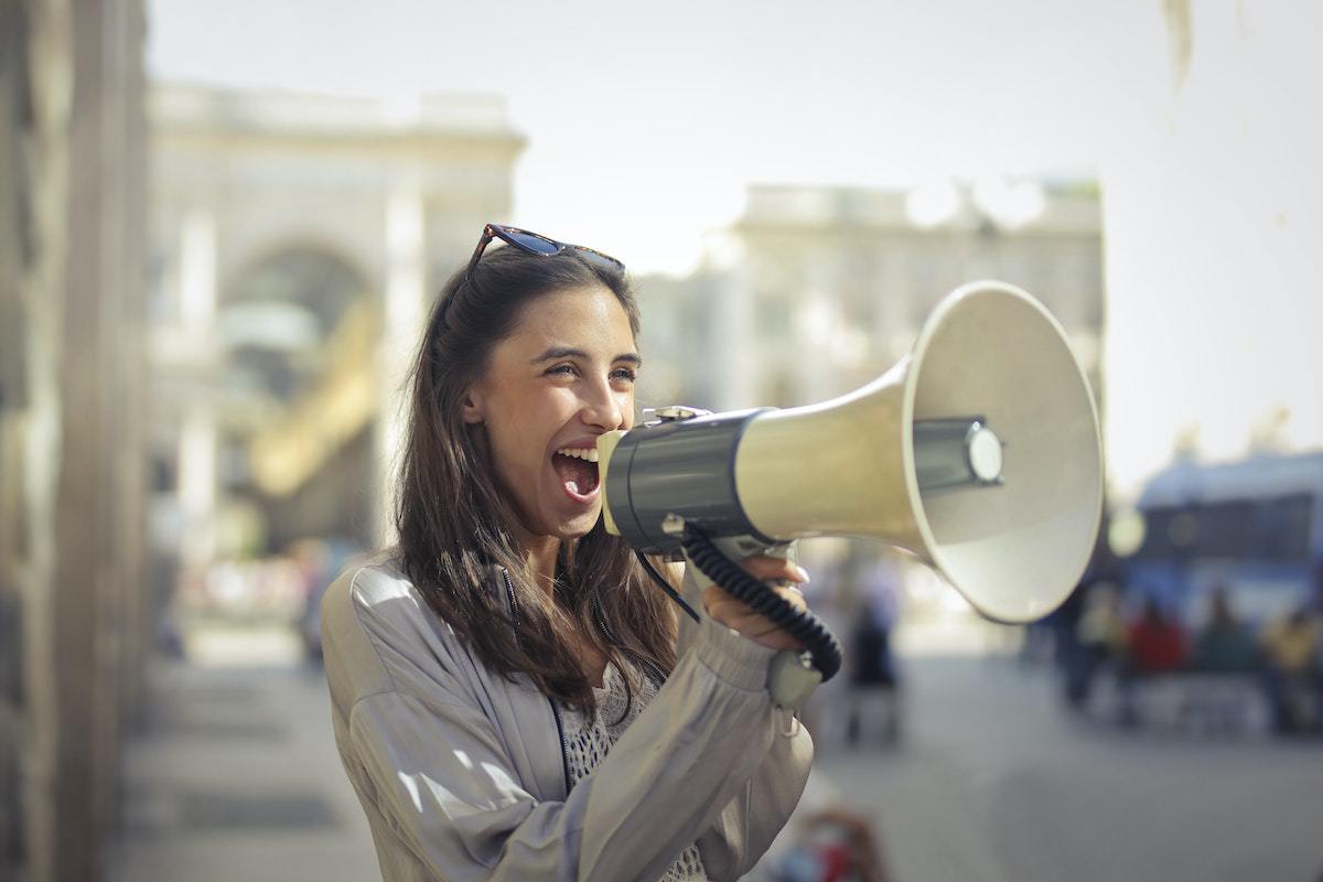 Megafone: Benefícios do marketing digital Mulher no meio da rua, como se estivesse em calçada, enquanto fala alto alguma coisa em seu megafone
